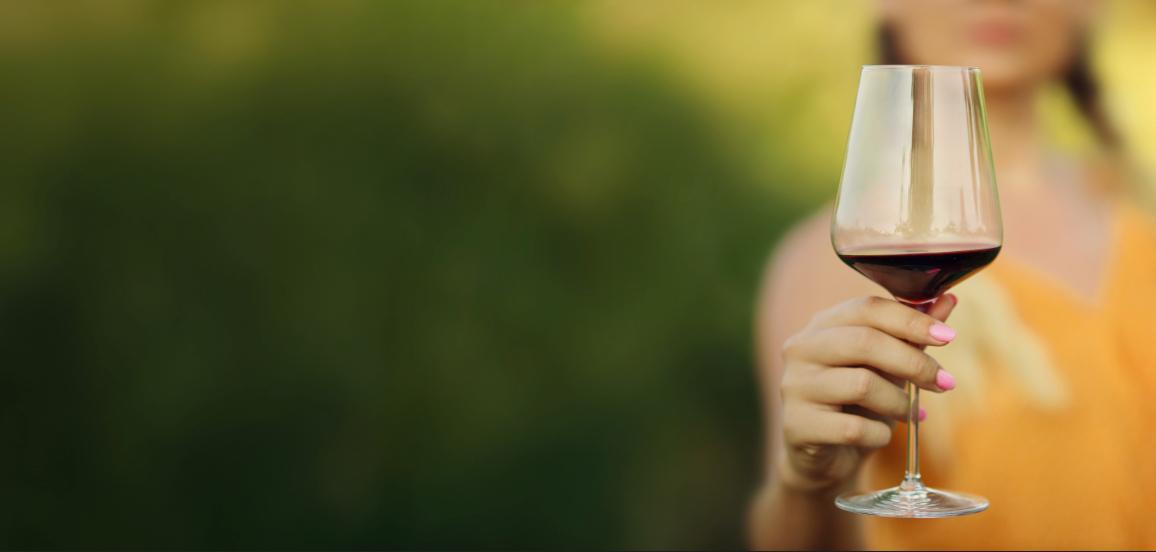 Person holding a glass of red wine with a blurred natural background