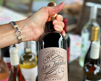 person holding red wine over table of other wines