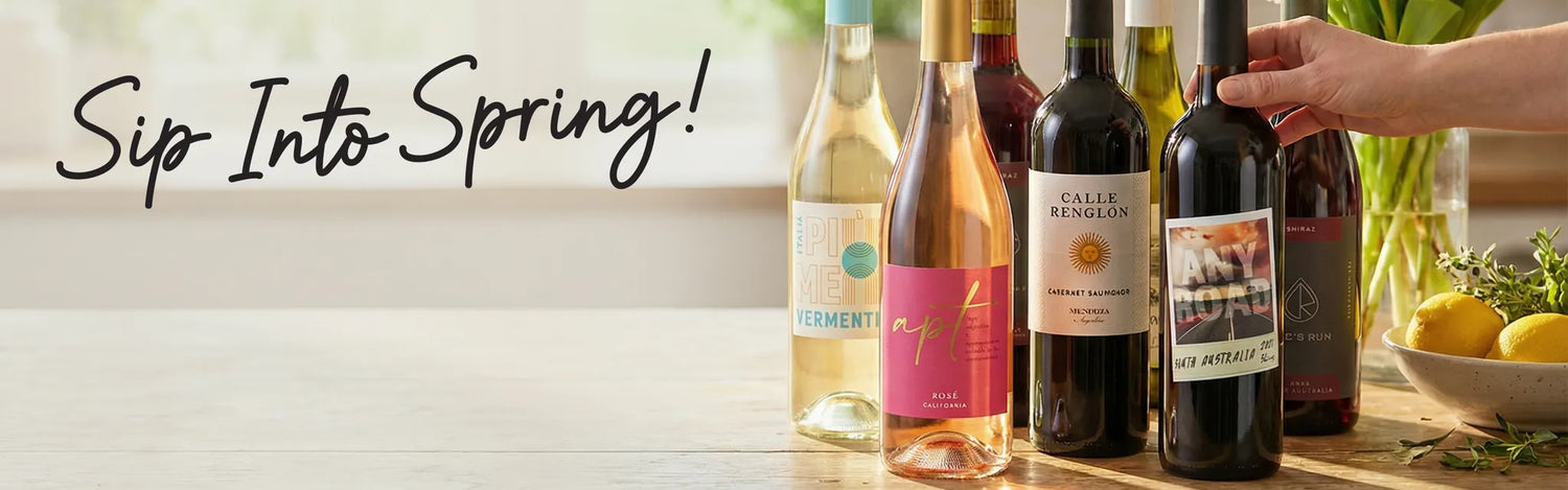 wood table with mixed wines, a hand reaching over a bowl of lemons to grab wine, black writing that says sip into spring