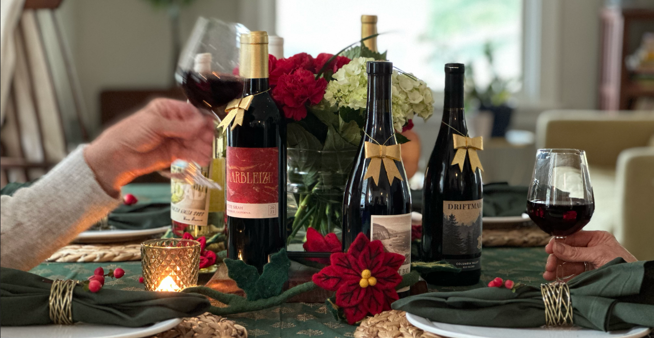 red wines with bows on a green holiday set table, with people lifting their glasses of red wine