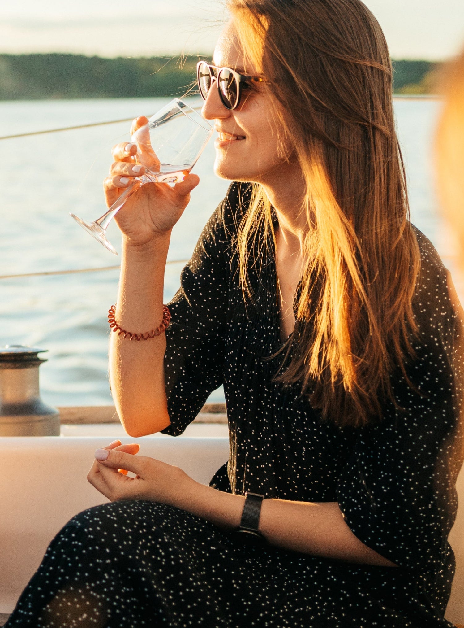 woman in polka-dotted dress and sunglasses sipping wine during sunset
