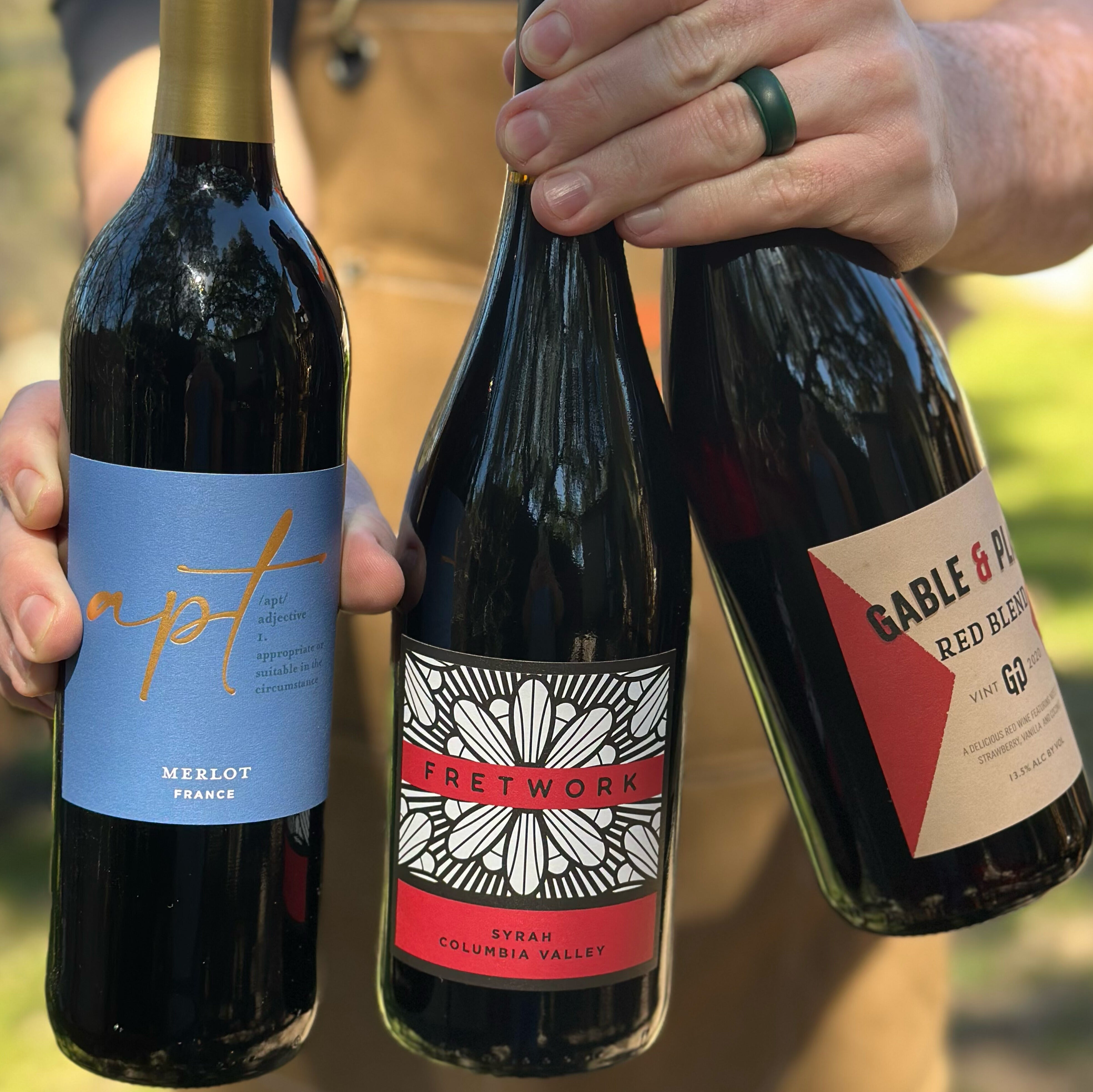three bottles of red wine held by person