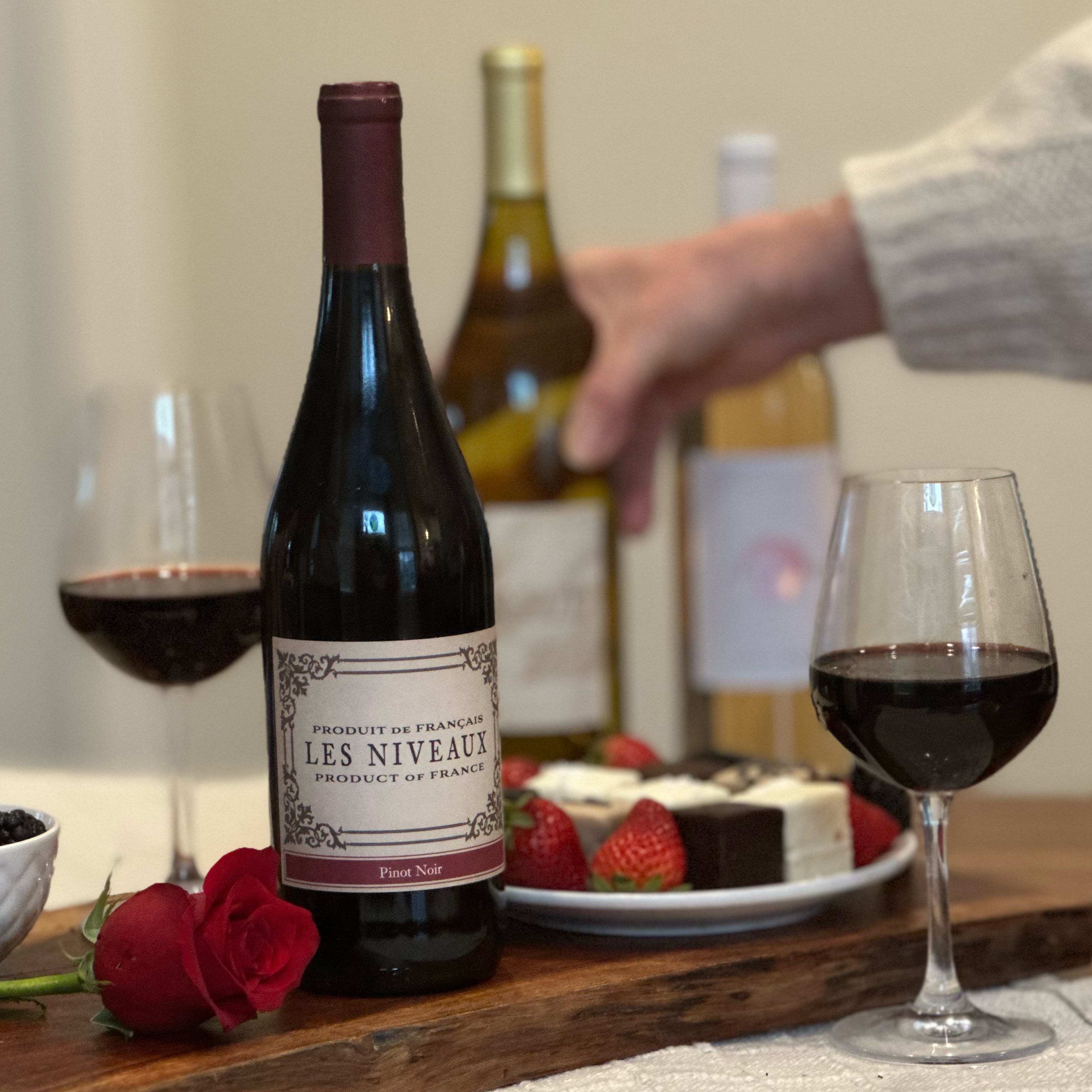 red, white and rose wines on serving board with roses, chocolates and strawberries